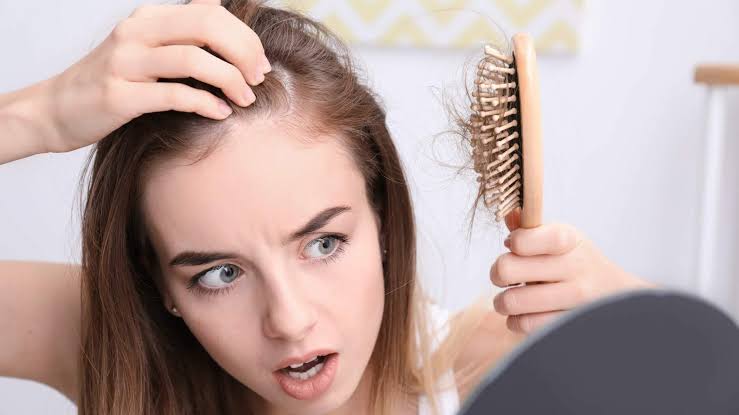 Woman noticing hair shedding in a hairbrush while checking her scalp